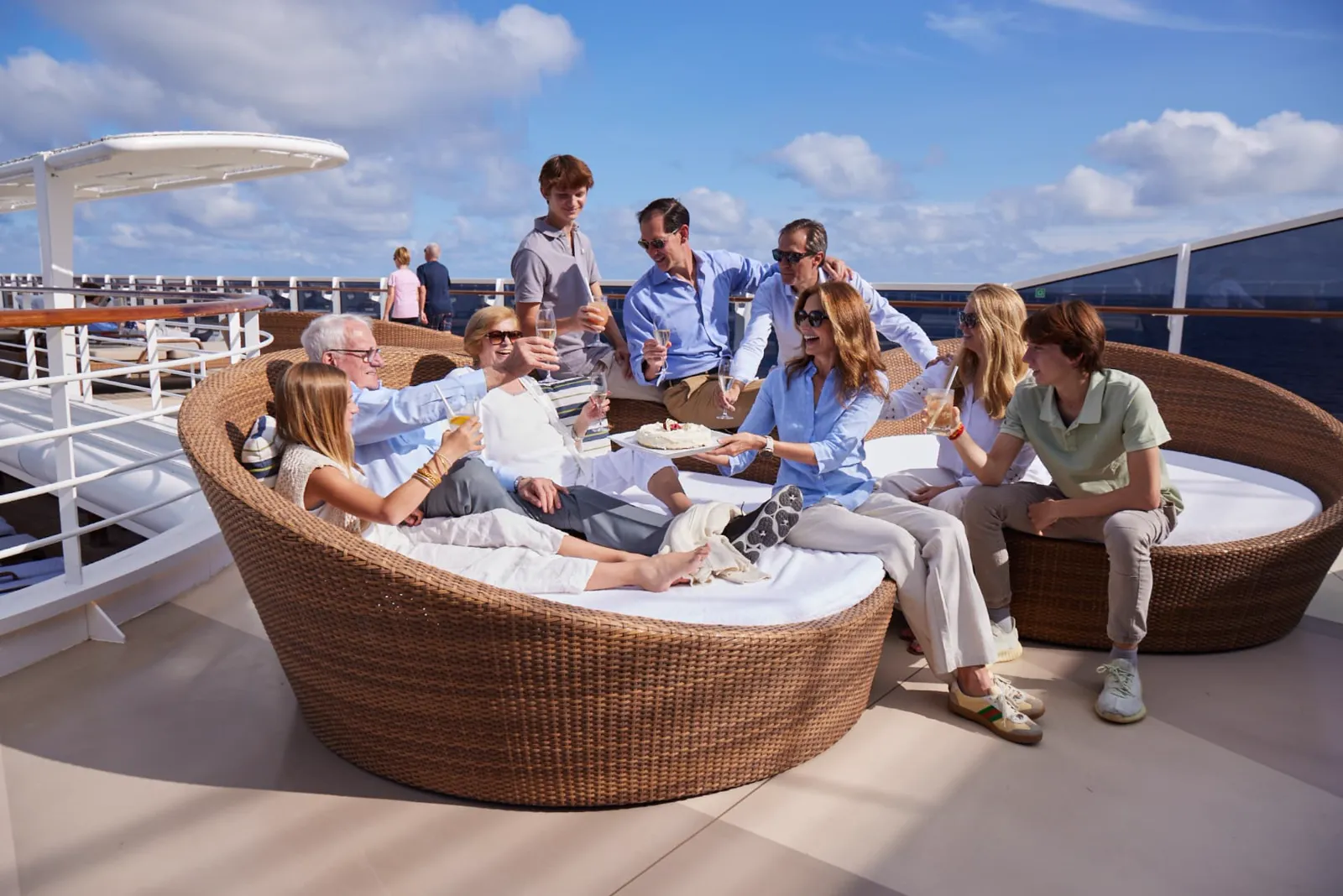 Three generations of a family toasting with drinks and serving cake on a cruise ship sun deck above the ocean