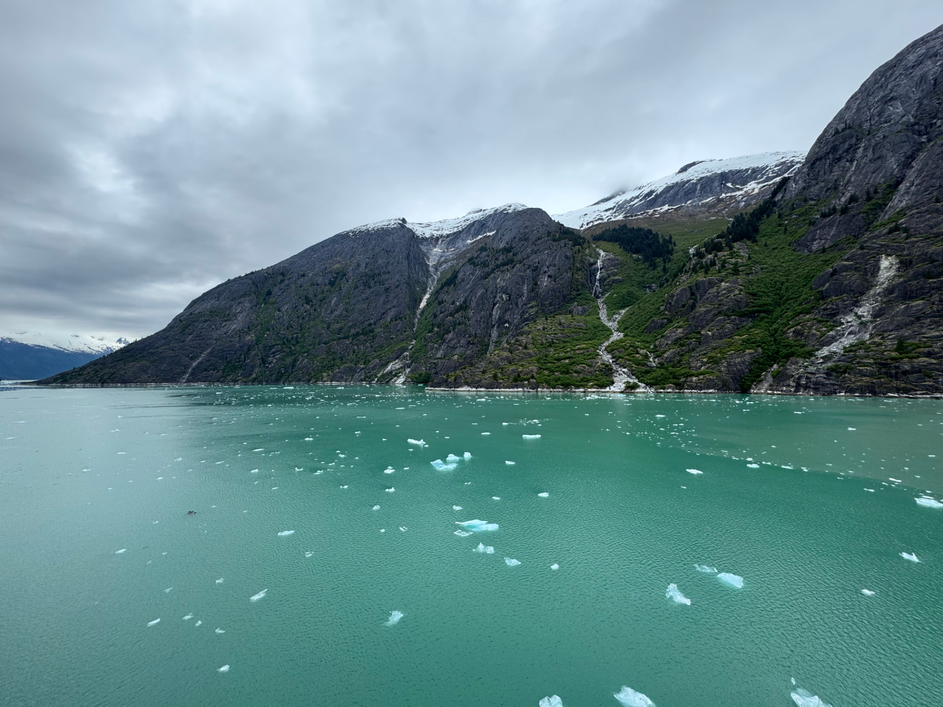 Turquoise Alaska inlet dotted with small icebergs beneath steep, snow-streaked mountains