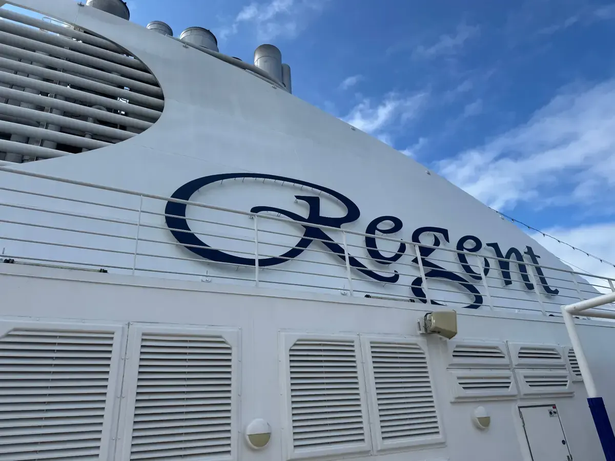 Regent Seven Seas Cruises name on the ship's funnel beneath a blue sky
