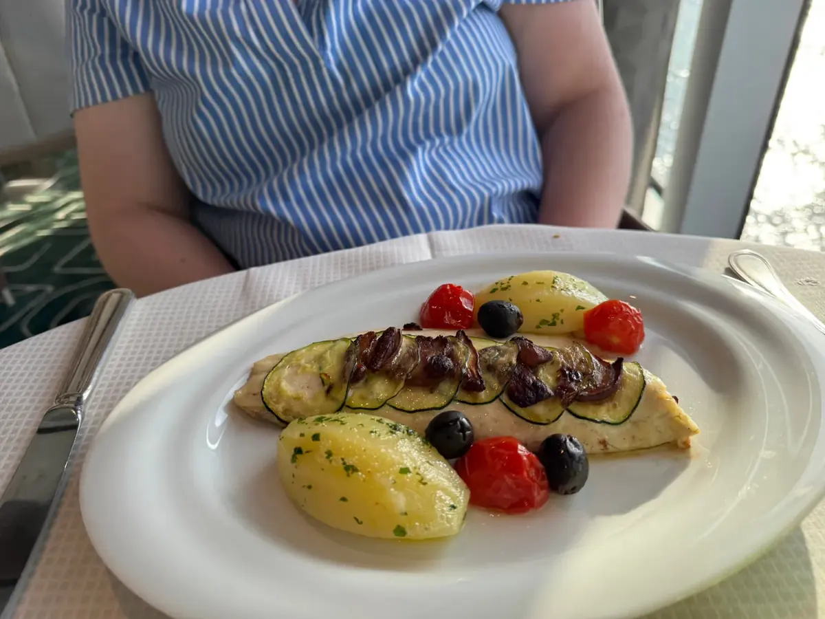 Baked fish topped with zucchini with potatoes, olives and tomatoes at Sette Mari